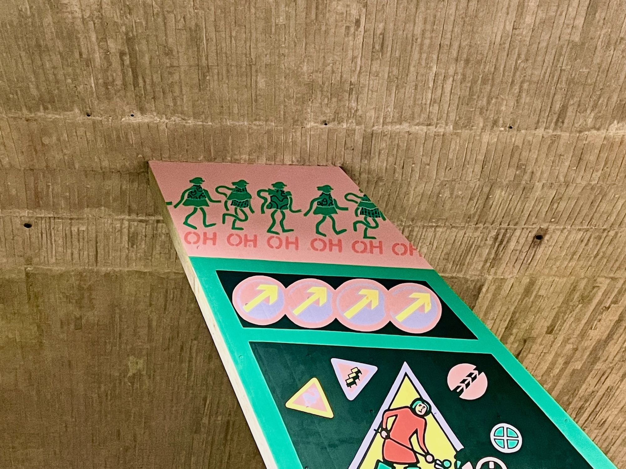 Part of a mural on a flyover pillar wall. A line of illustrated green people walking in a line on a pink background. The word "OH" is under each of them.