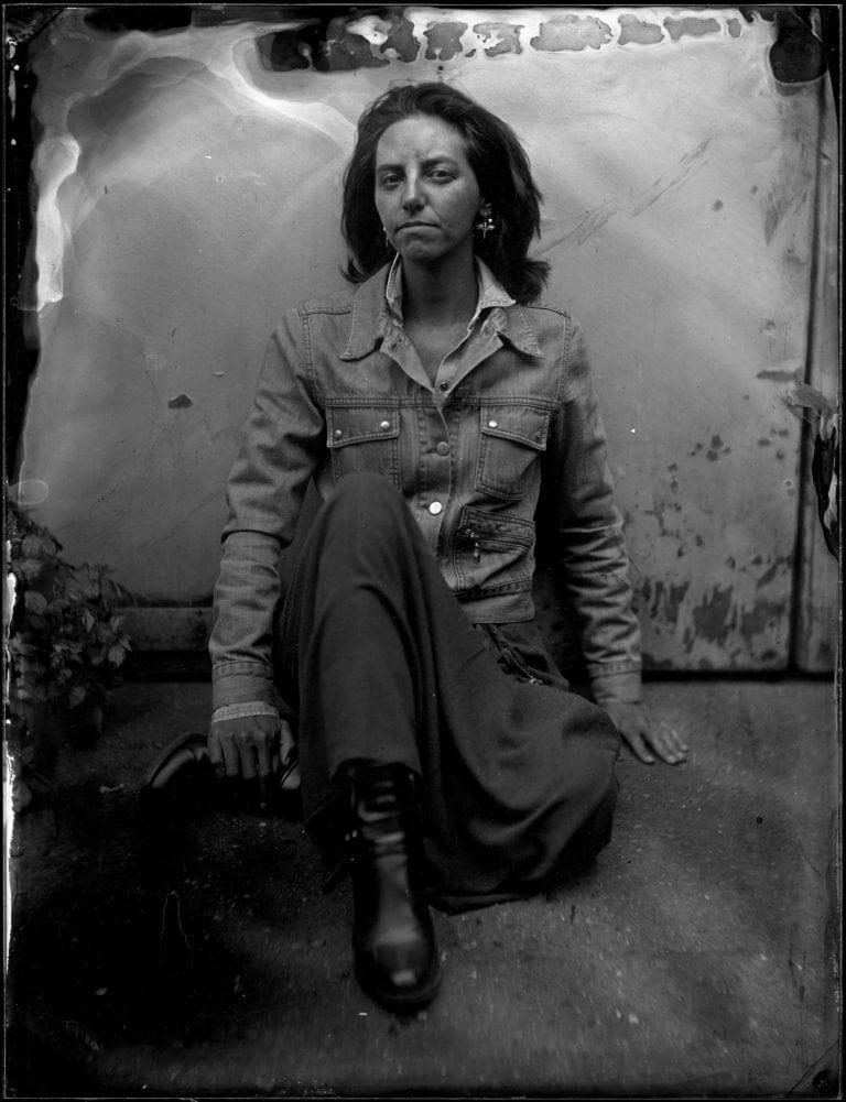 A woman sits on the ground with one leg tucked under. She is resting one hand on her boot.