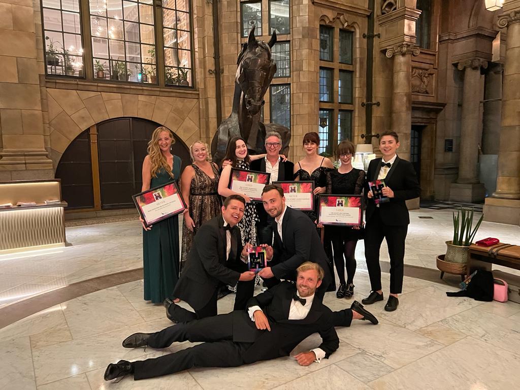 The AUB Marketing Team at HEIST Awards 2022 holding up certificates and a trophy in a foyer.