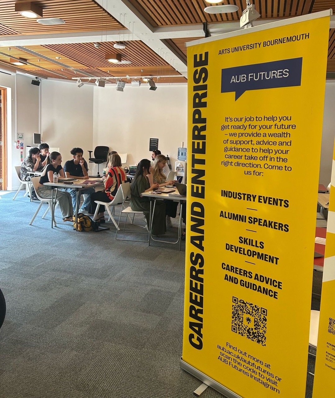 Students in a large room talking to industry professionals, large yellow banner in front.