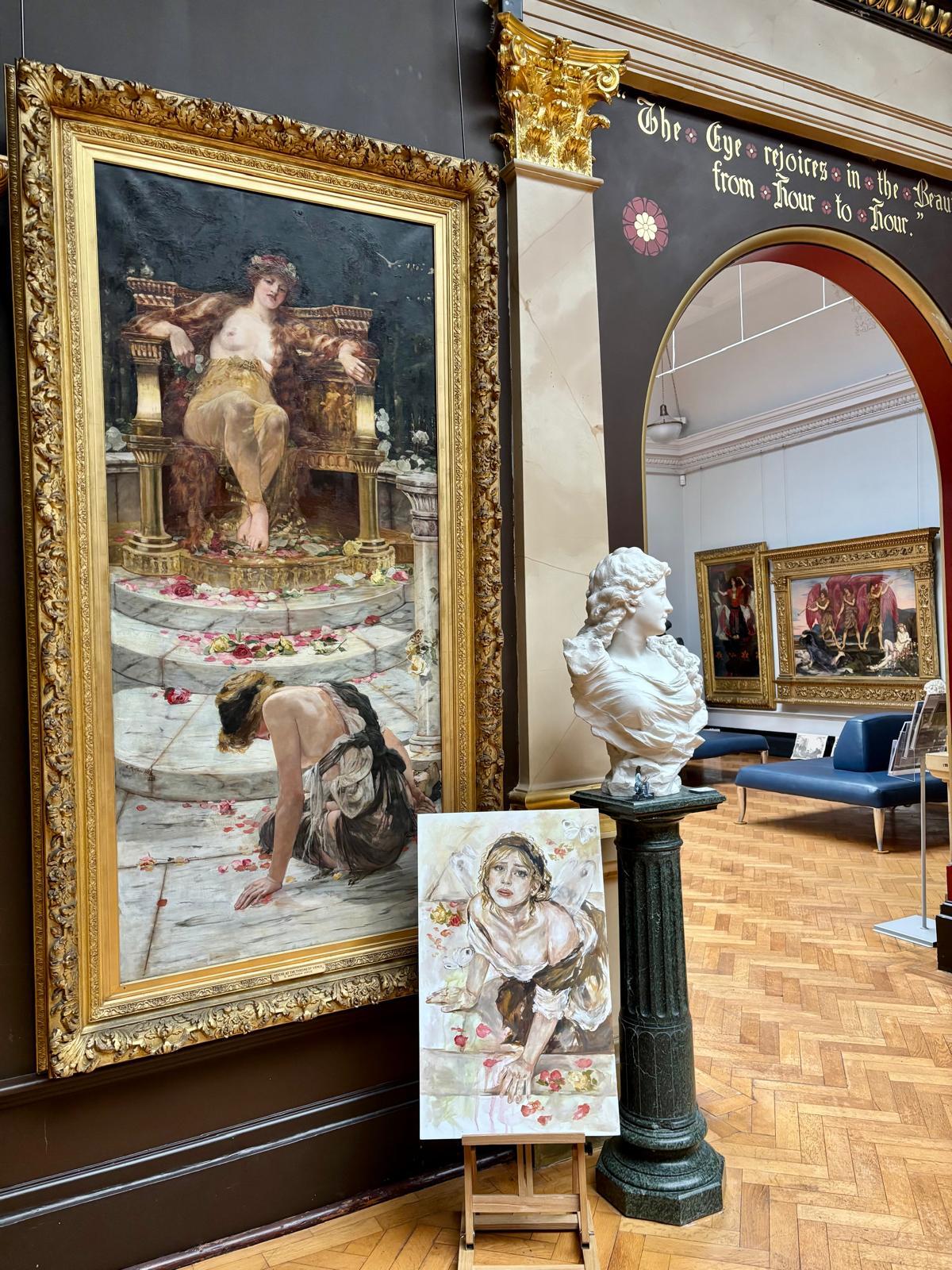 Museum gallery with ornate gold-framed classical painting, white marble bust on green column, wooden parquet flooring, and arched doorway.