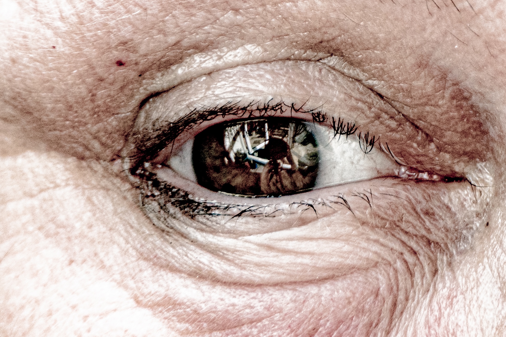 A close-up of one eye on a person’s face, with wrinkles around the eyelid and a reflection visible in the pupil.
