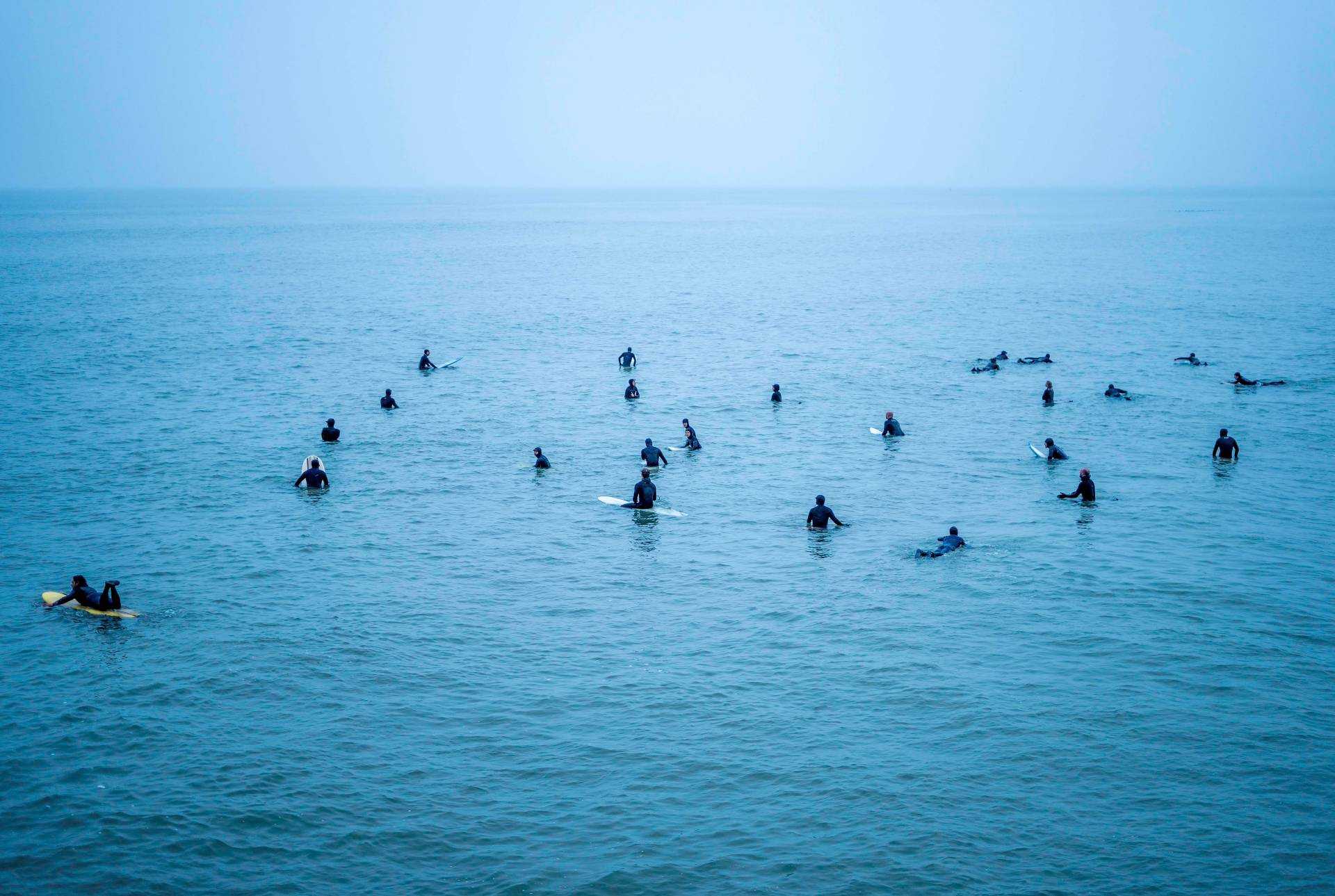 A large group of surfers on boards in open water.