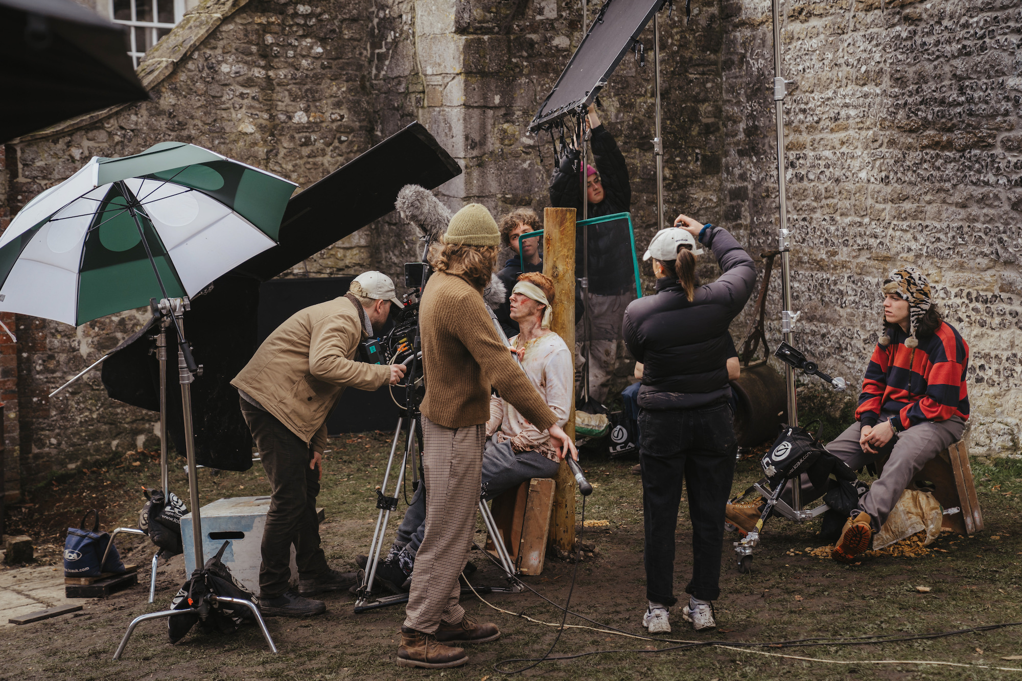Camera crew setting up equipment to film in castle ruins, model with injury prosthetics and dirty.