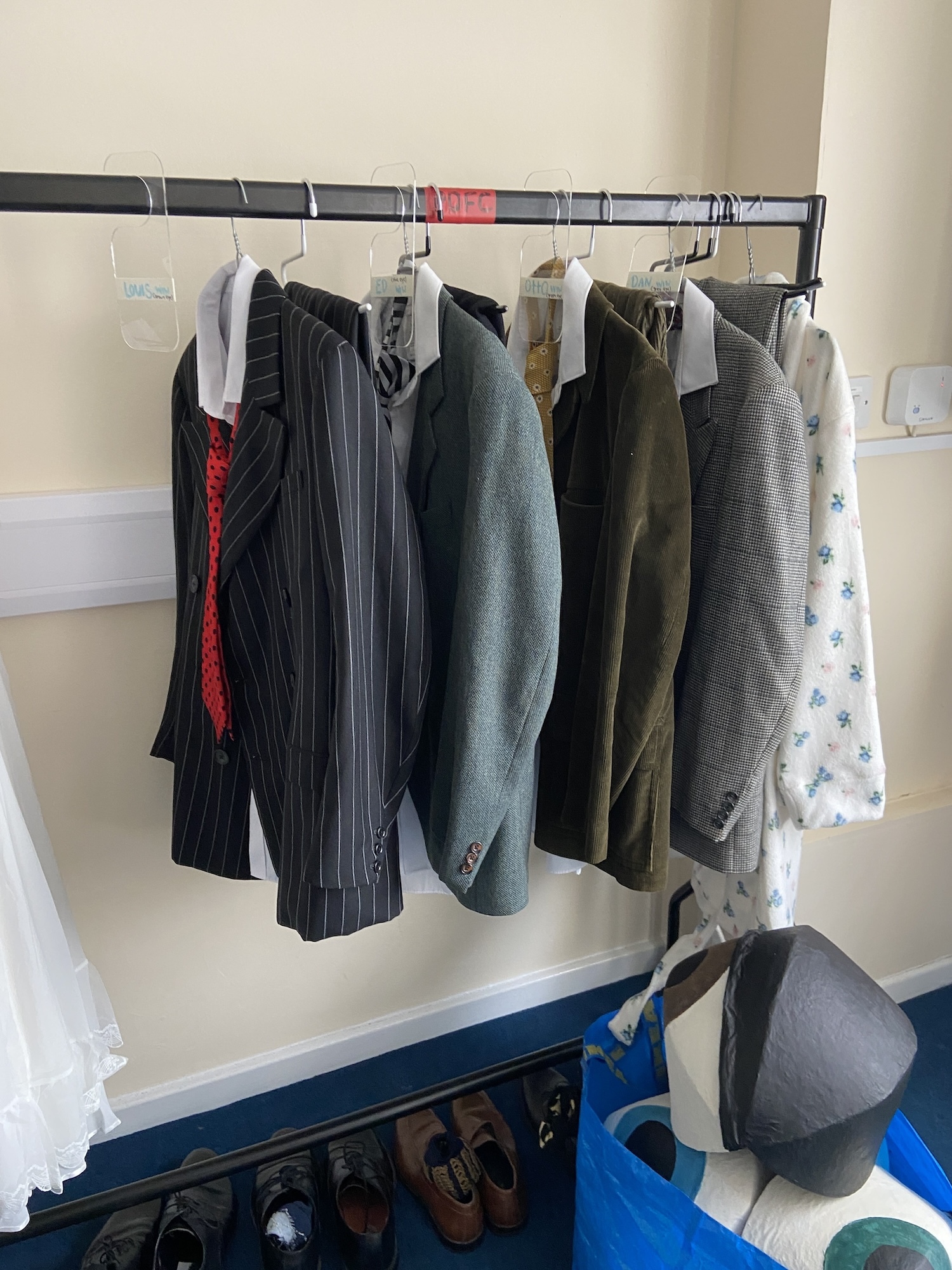 Four men's suit jackets, shirts and ties hanging on hangers on a costume rail.