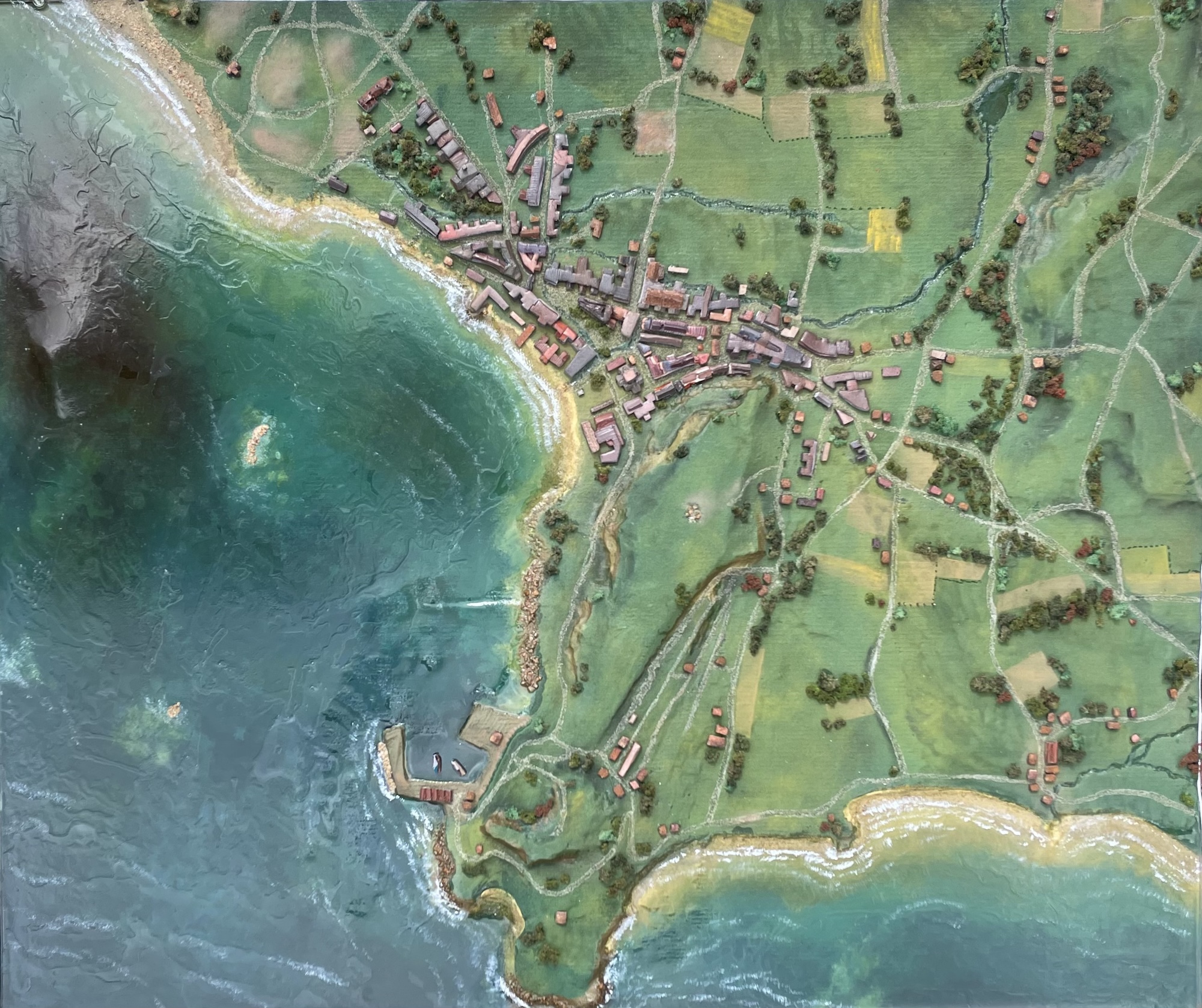 Overhead diorama showing green fields and surrounding towns, with a coastline and blue water surrounding it.