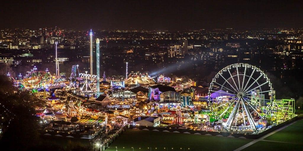 A massive bright and colourfully lit fairground viewed at night with a cityscape in the background.
