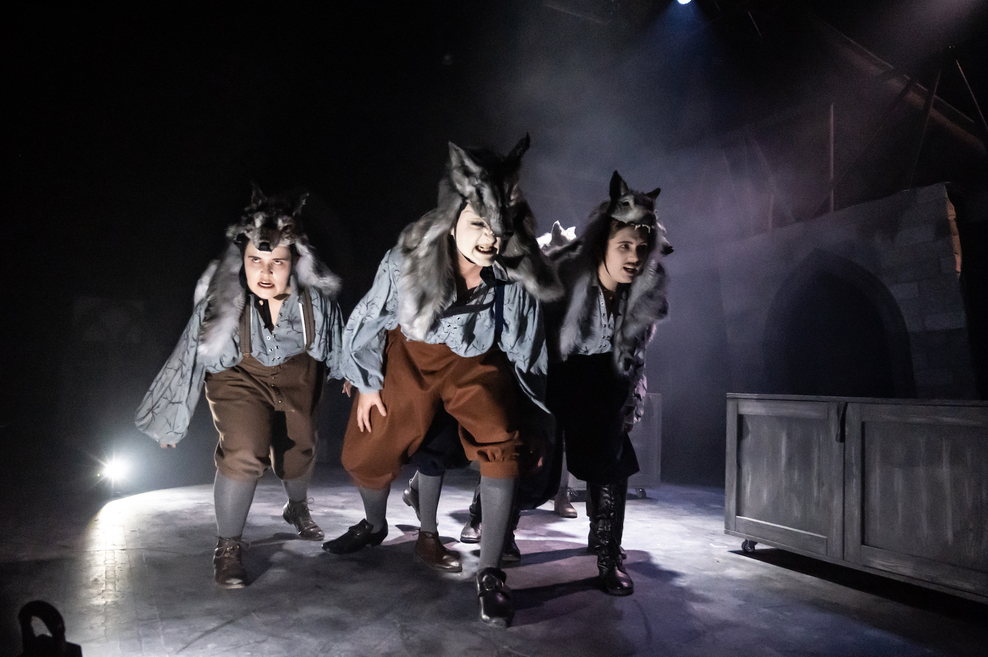 A group of actors wearing wolf-like costumes on stage.