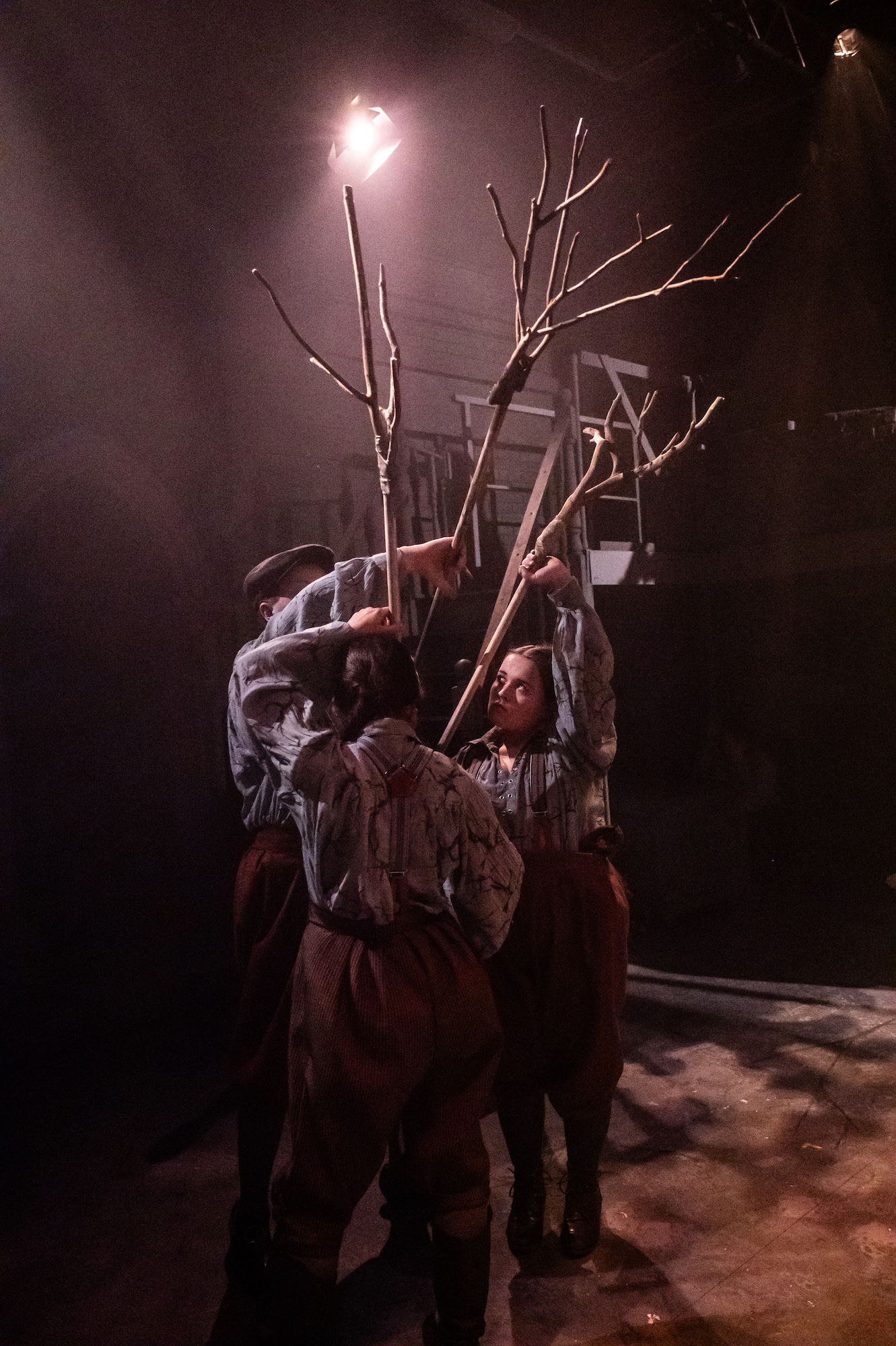 A group of actors holding up tree branches under the stage lights.