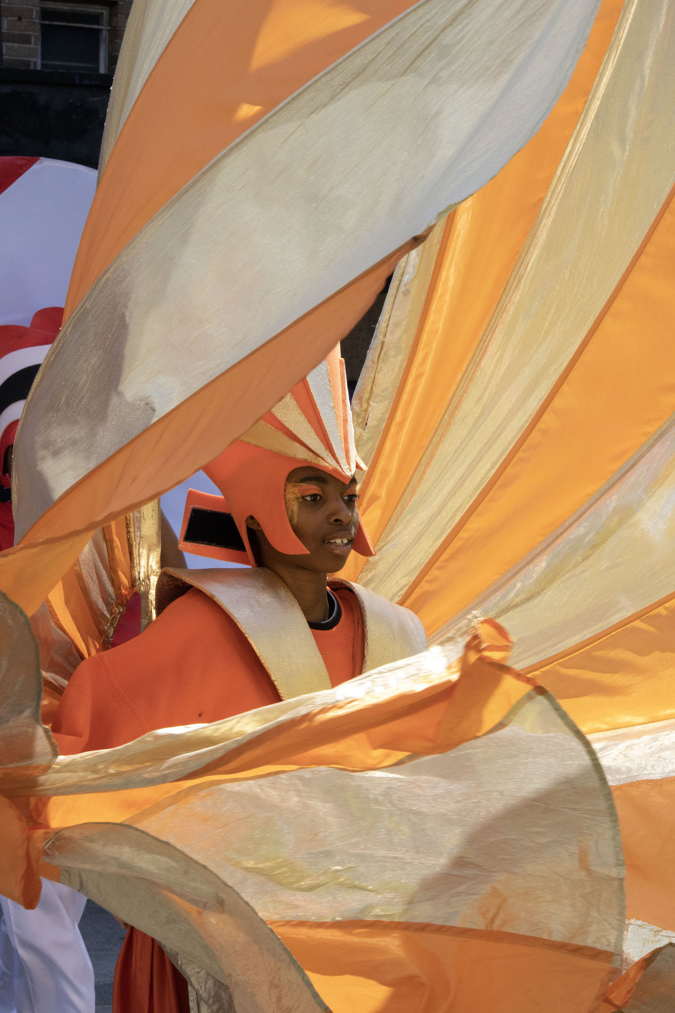 A person in a massive orange and pale yellow-coloured costume in a carnival parade.