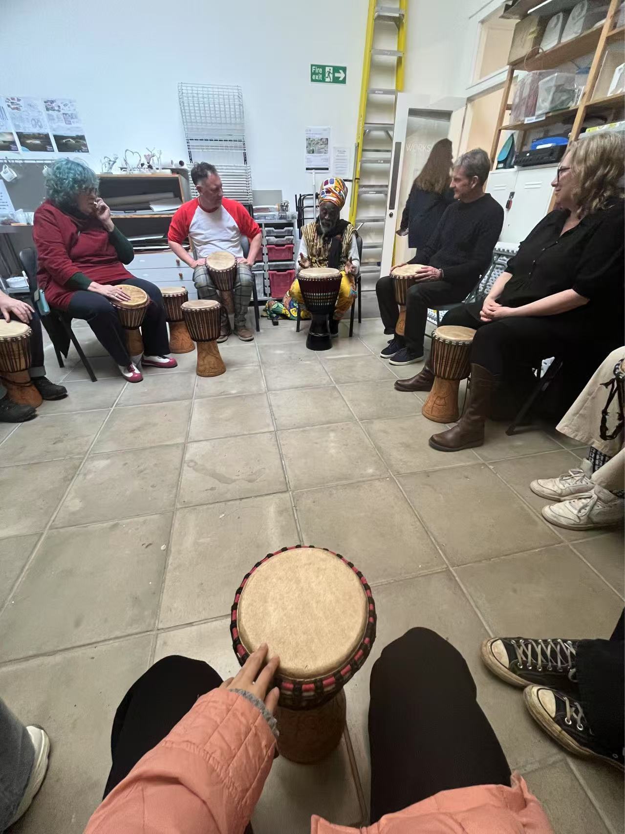 A circle of MA Fine Art students and staff with African drums in front of them, taking part in an African drumming workshop.