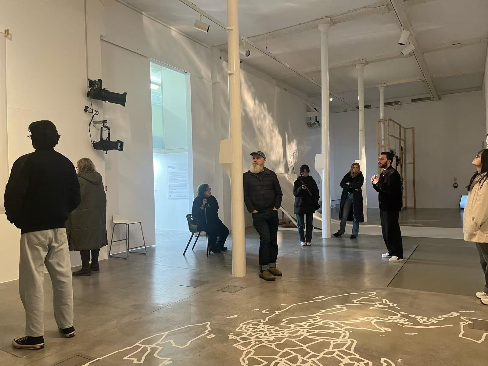 A group of MA Fine Art students standing in a large spacious gallery space looking at an exhibition.