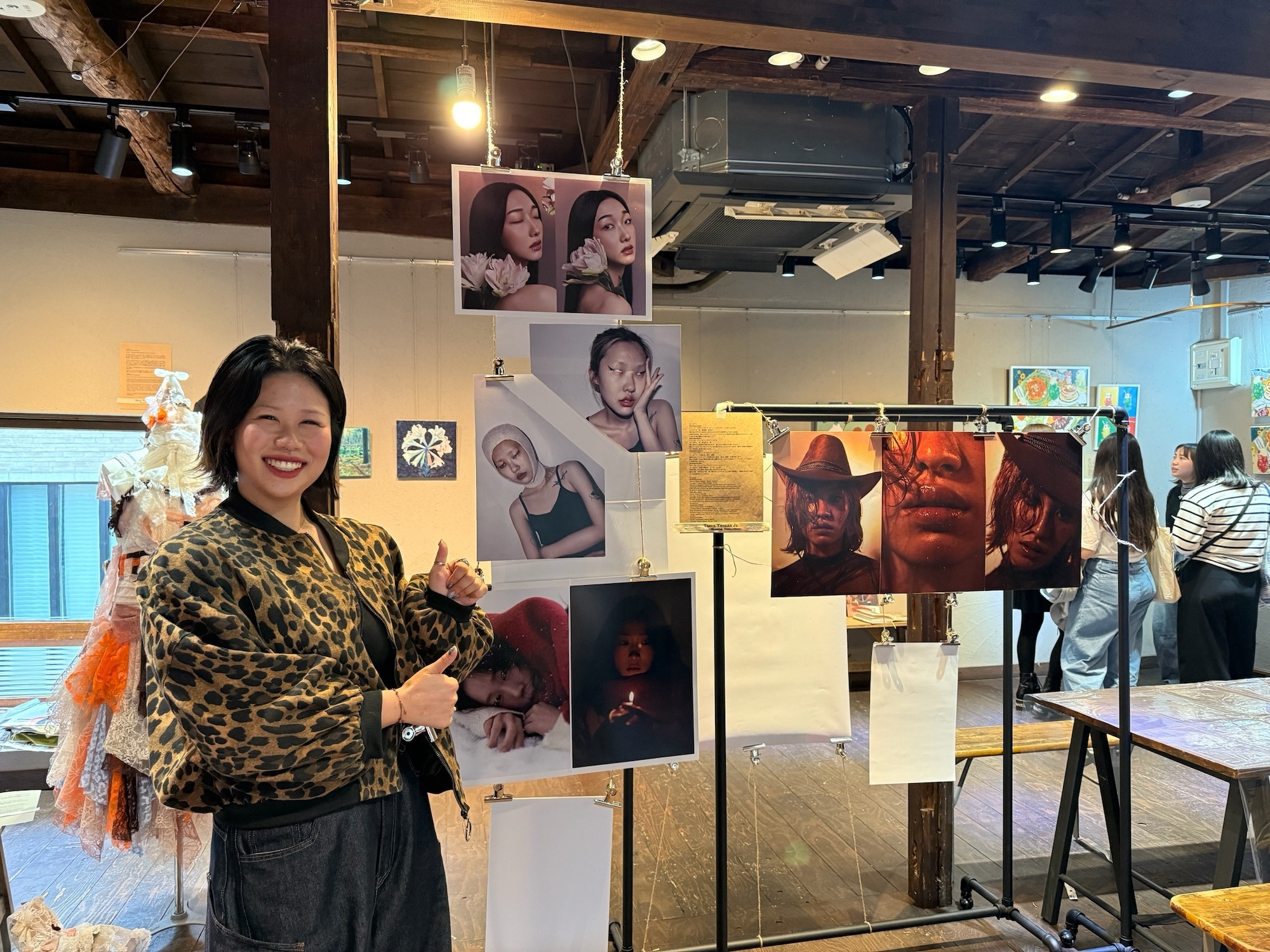Woman in leopard print jacket holding flowers stands beside art exhibition display with portrait photographs mounted on stands.