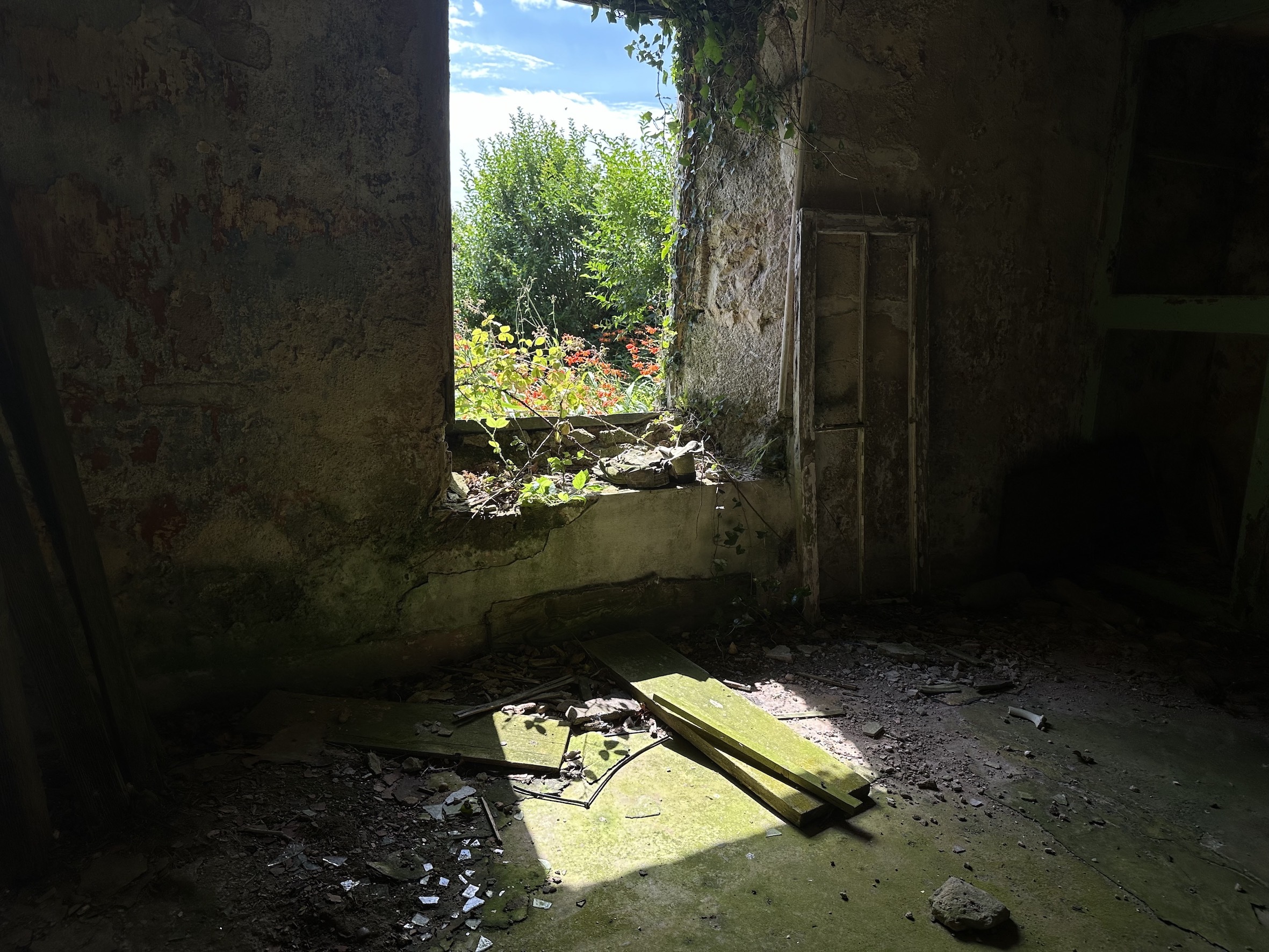 Film still showing a window of an old, derelict stone building, with bright sunlight and greenery visible outside.