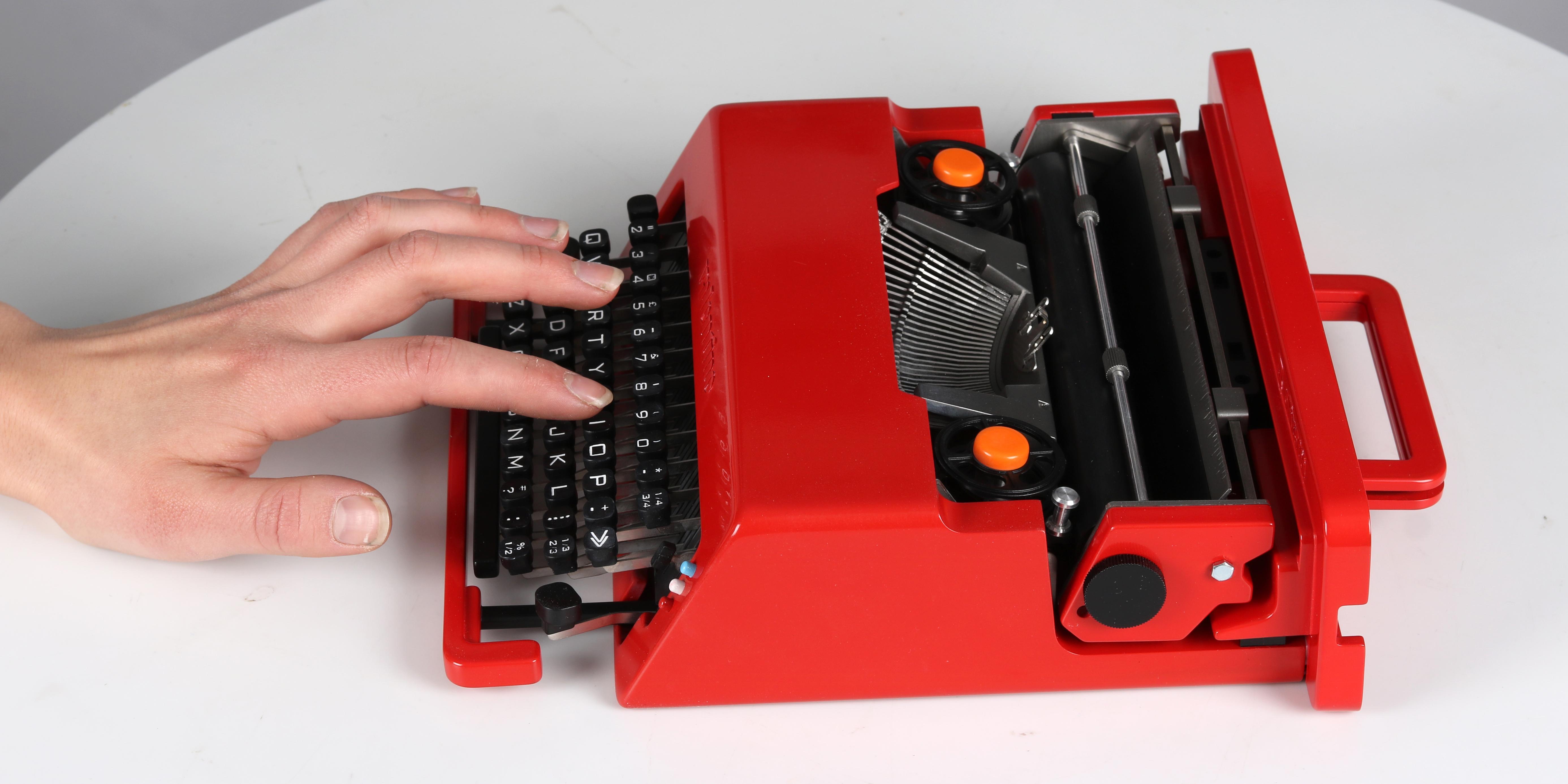 A miniature typewriter resting on a table with a hand touching the keys.