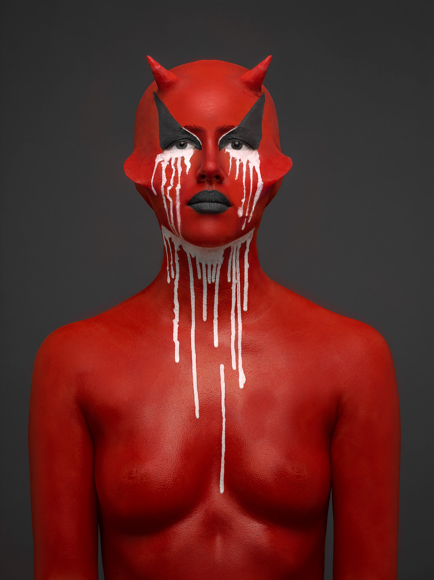 A nude figure with facial prosthetics and white paint dripping from their eyes and neck.