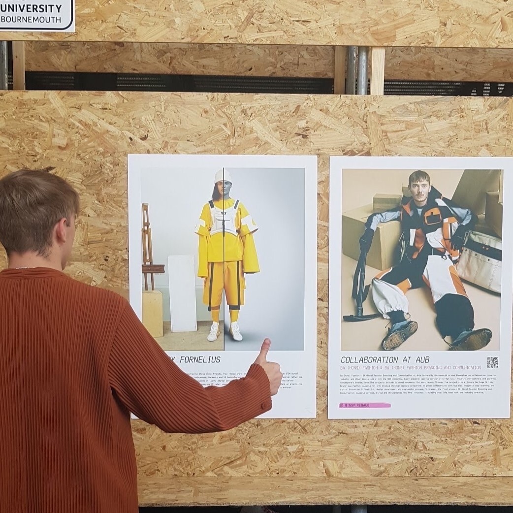 Person in red jumper viewing two posters on wooden wall - left shows yellow protective suit, right shows person in laboratory