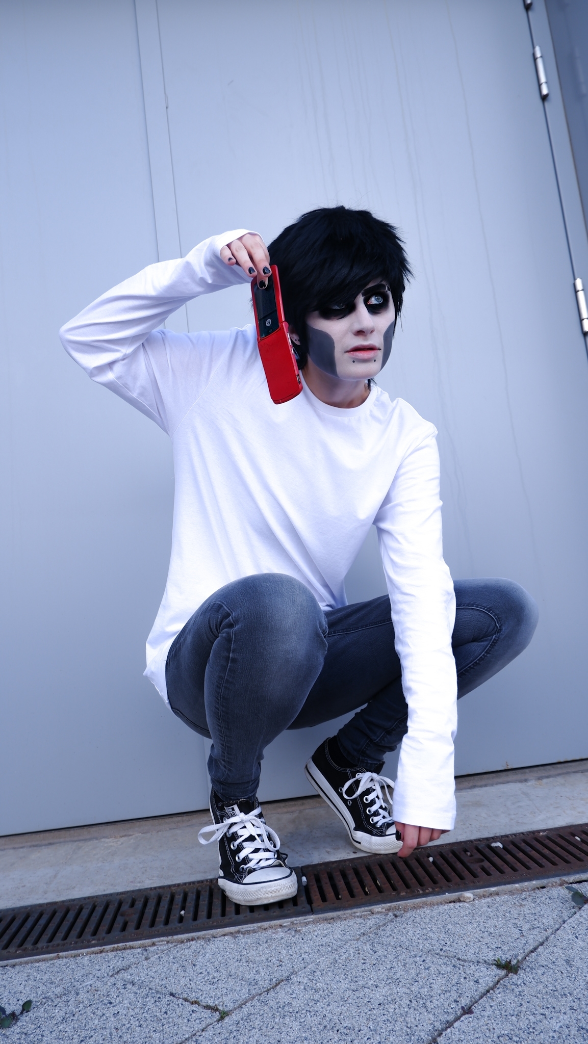 A person is crouching down; they're dressed in a white long sleeve T-shirt and grey jeans.