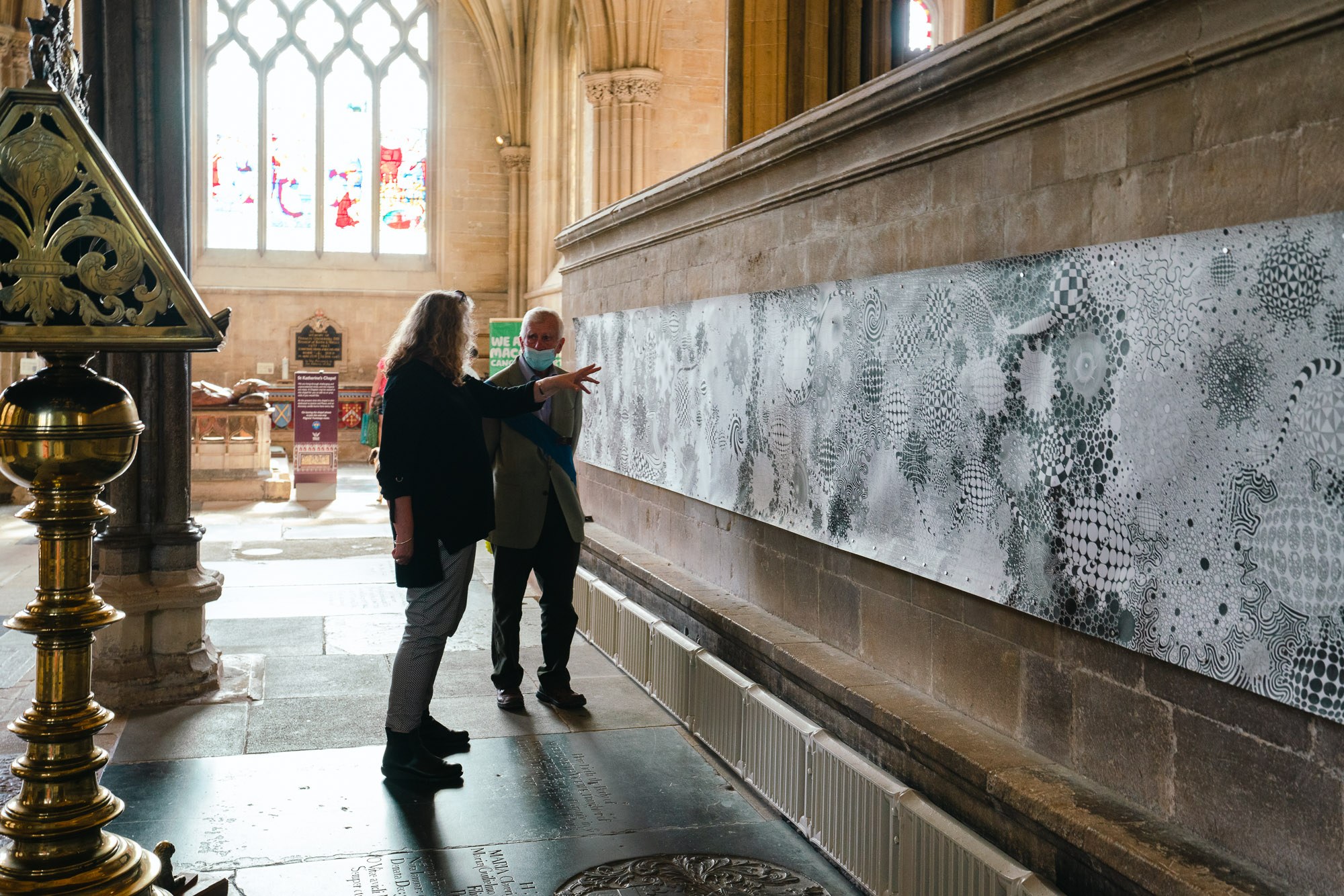 People stand and look at a long landscape canvas hanging on a cathedral wall.