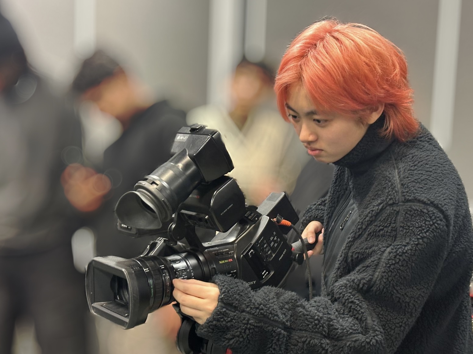 MA Film Practice student Z Chu holding a film camera. Other students are blurred out in the background.