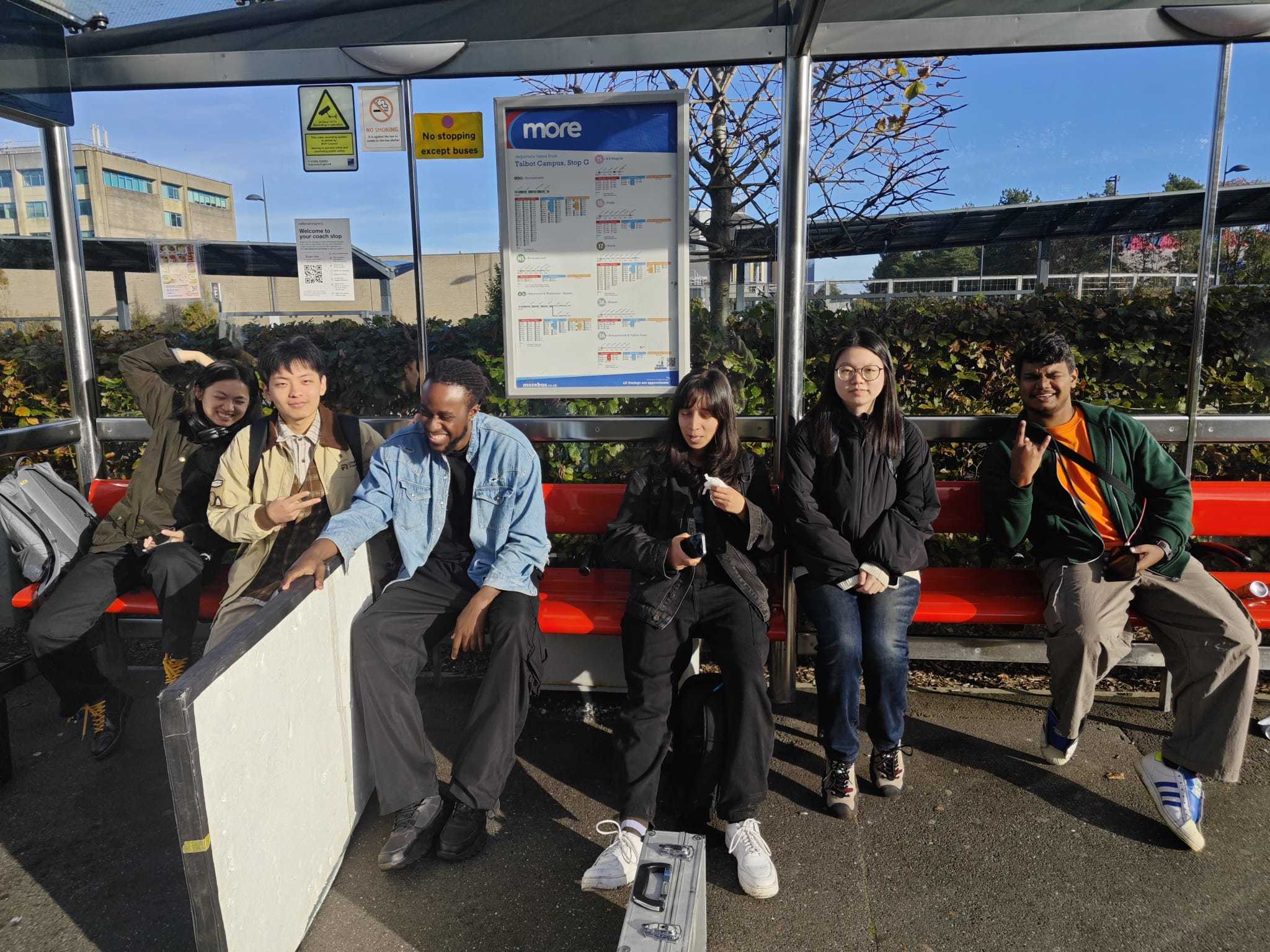 A group of six MA Film Practice students sitting under a bus shelter near Arts University Bournemouth campus.