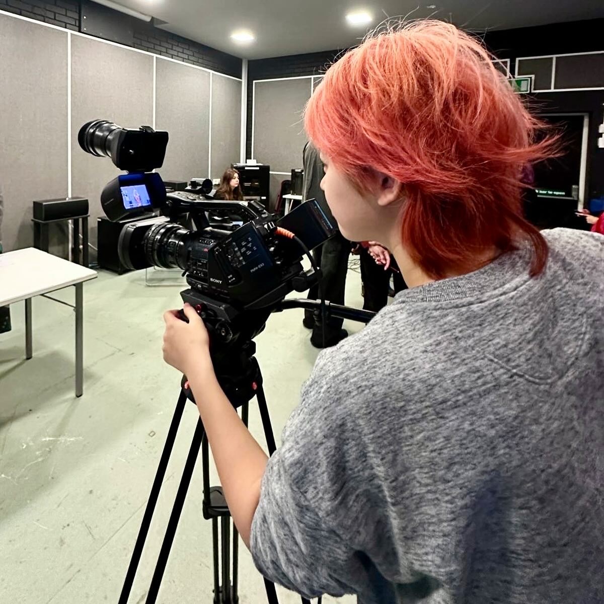 MA Film Practice student Z Chu viewed from behind, standing behind a camera and tripod in a studio.