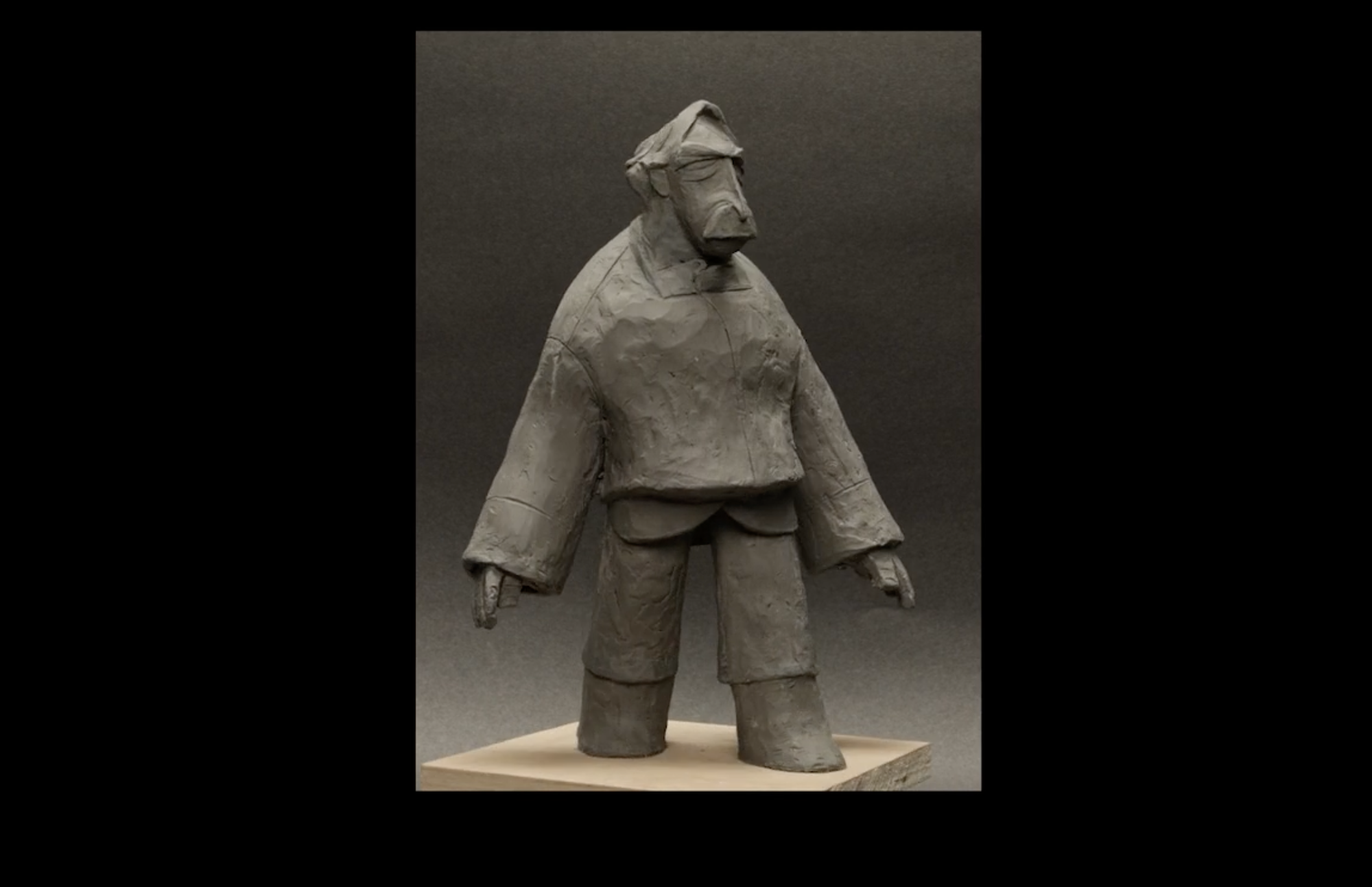 Clay model sculpture of male character with long arms, hair and moustache, dark background.