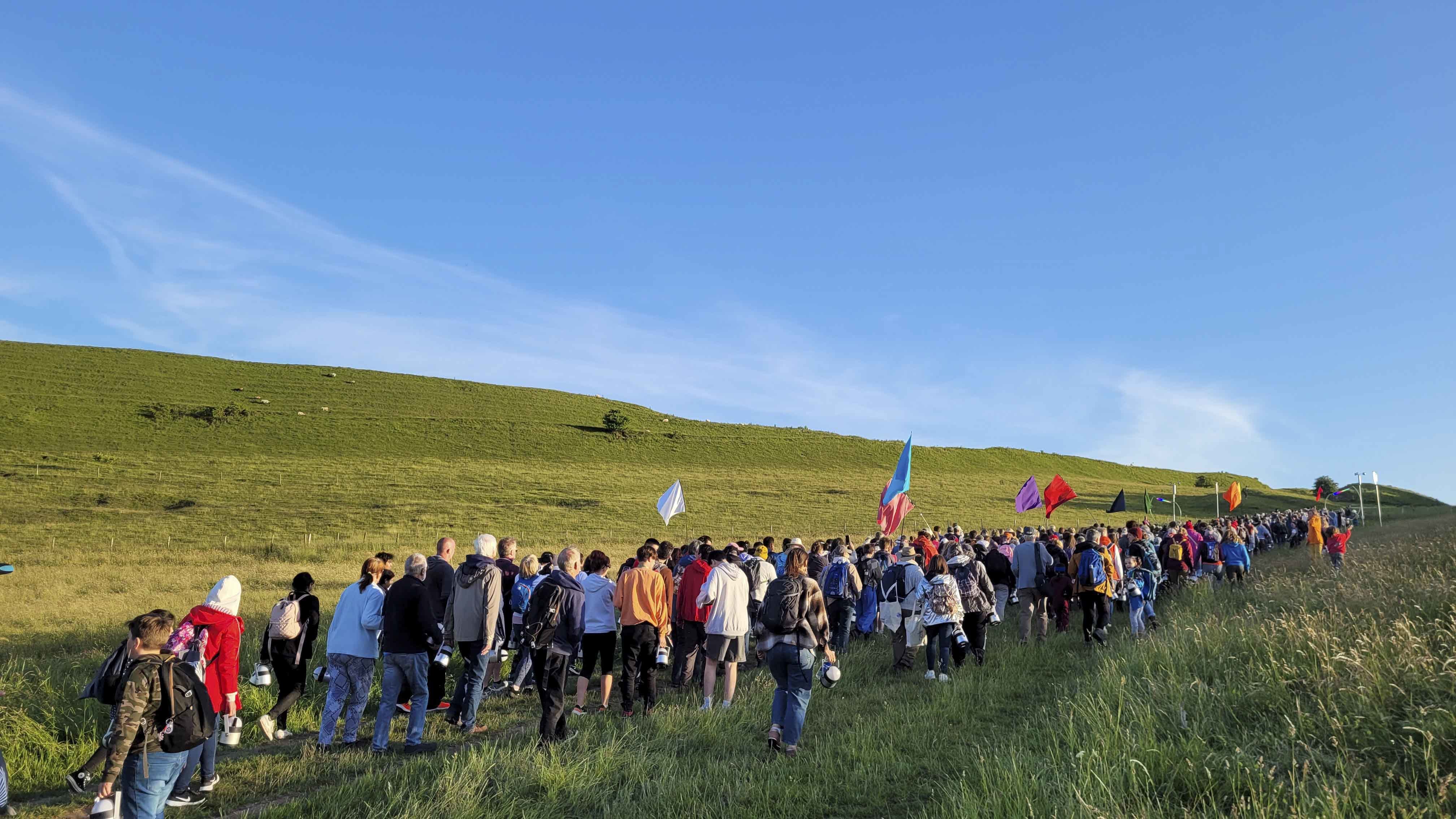 A large crowd of people walks across a large field with a blue sky overhead