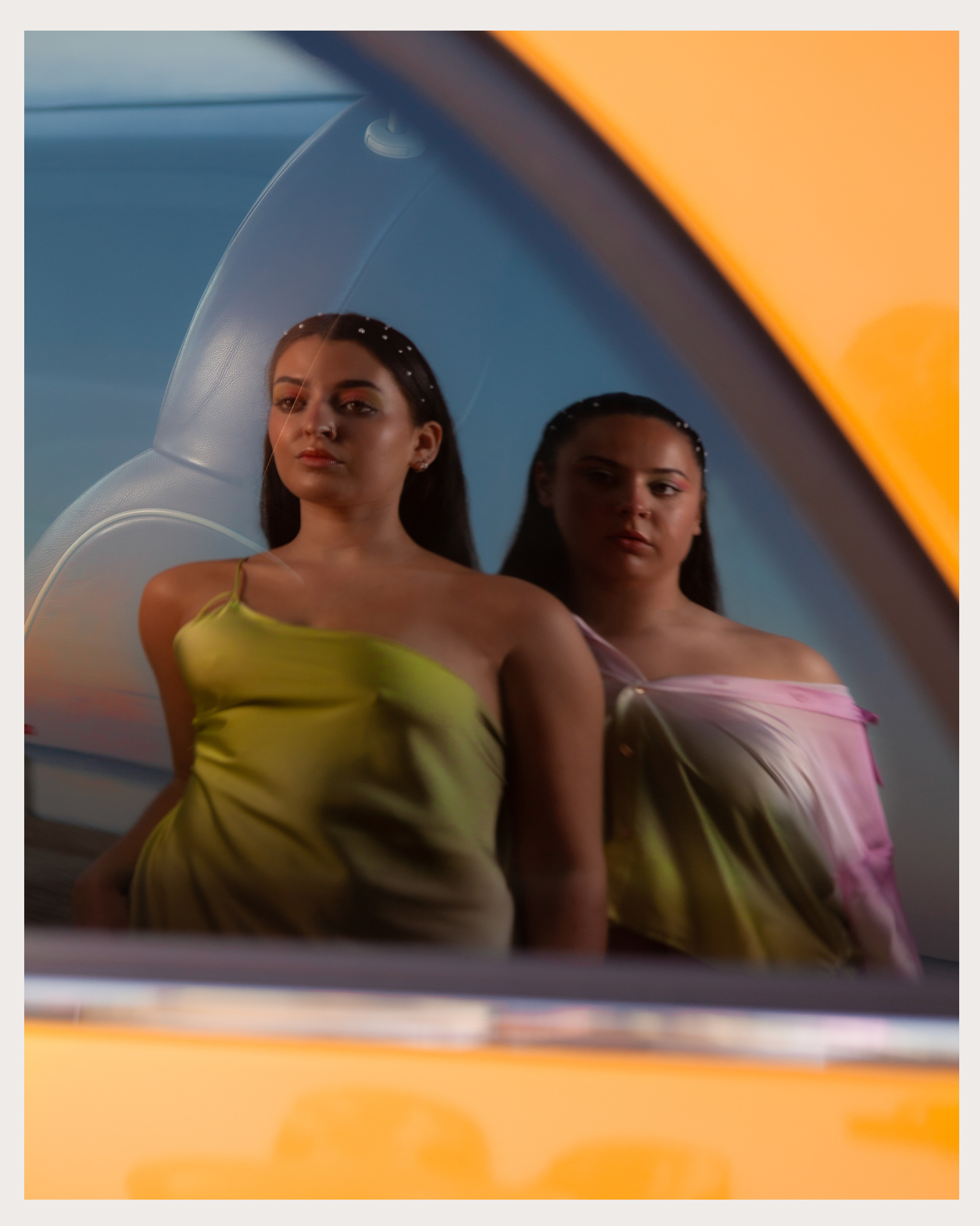 Two models and a sunset sky reflected in a car window.