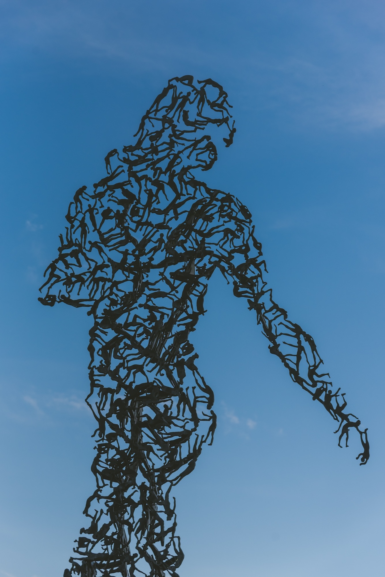Several small human silhouettes placed together to form a larger human figure looking around to the right with one arm stretched out, with a blue sky background.