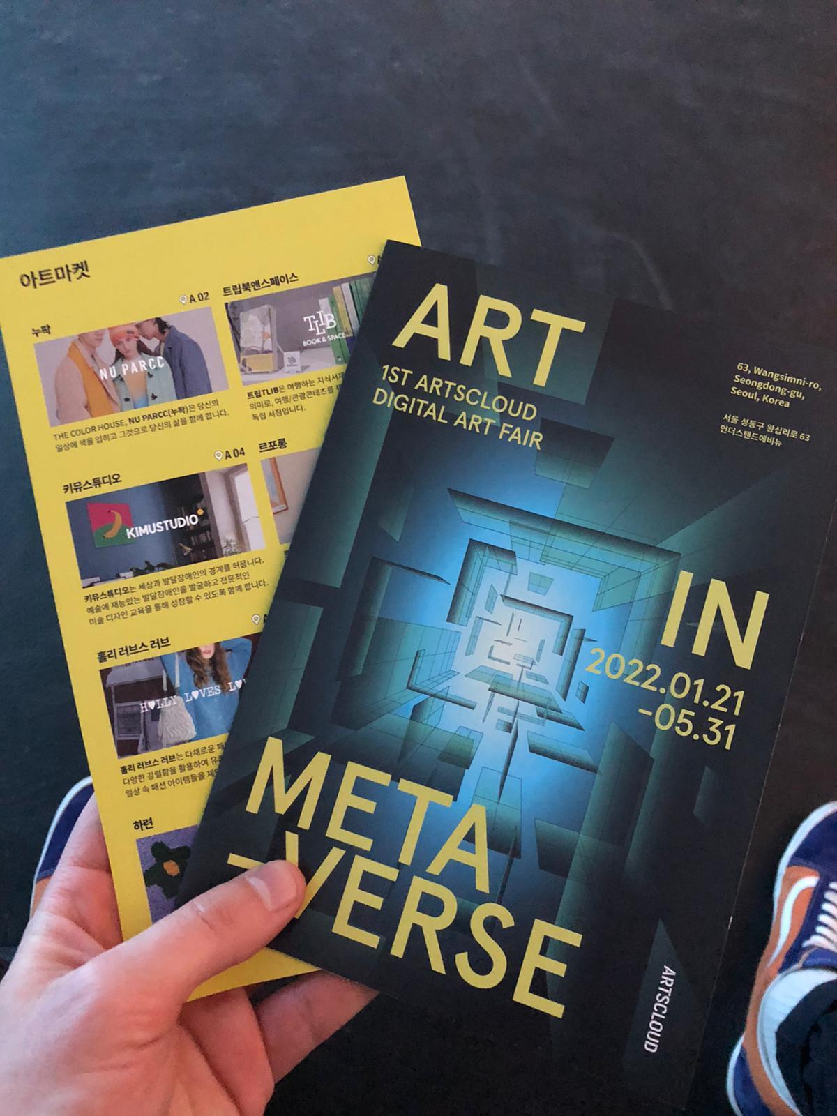 A hand holding flyers for an art exhibition