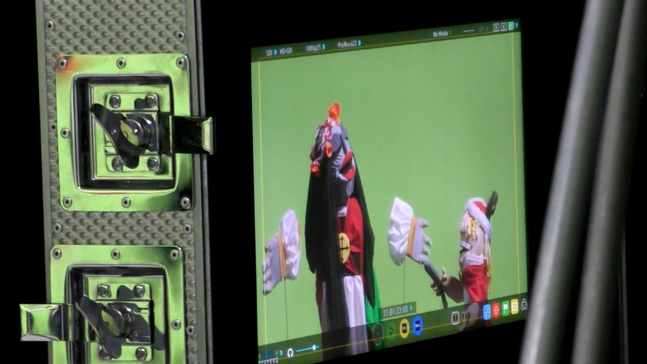 Close-up of a film camera monitor, showing two puppets performing against a greenscreen.