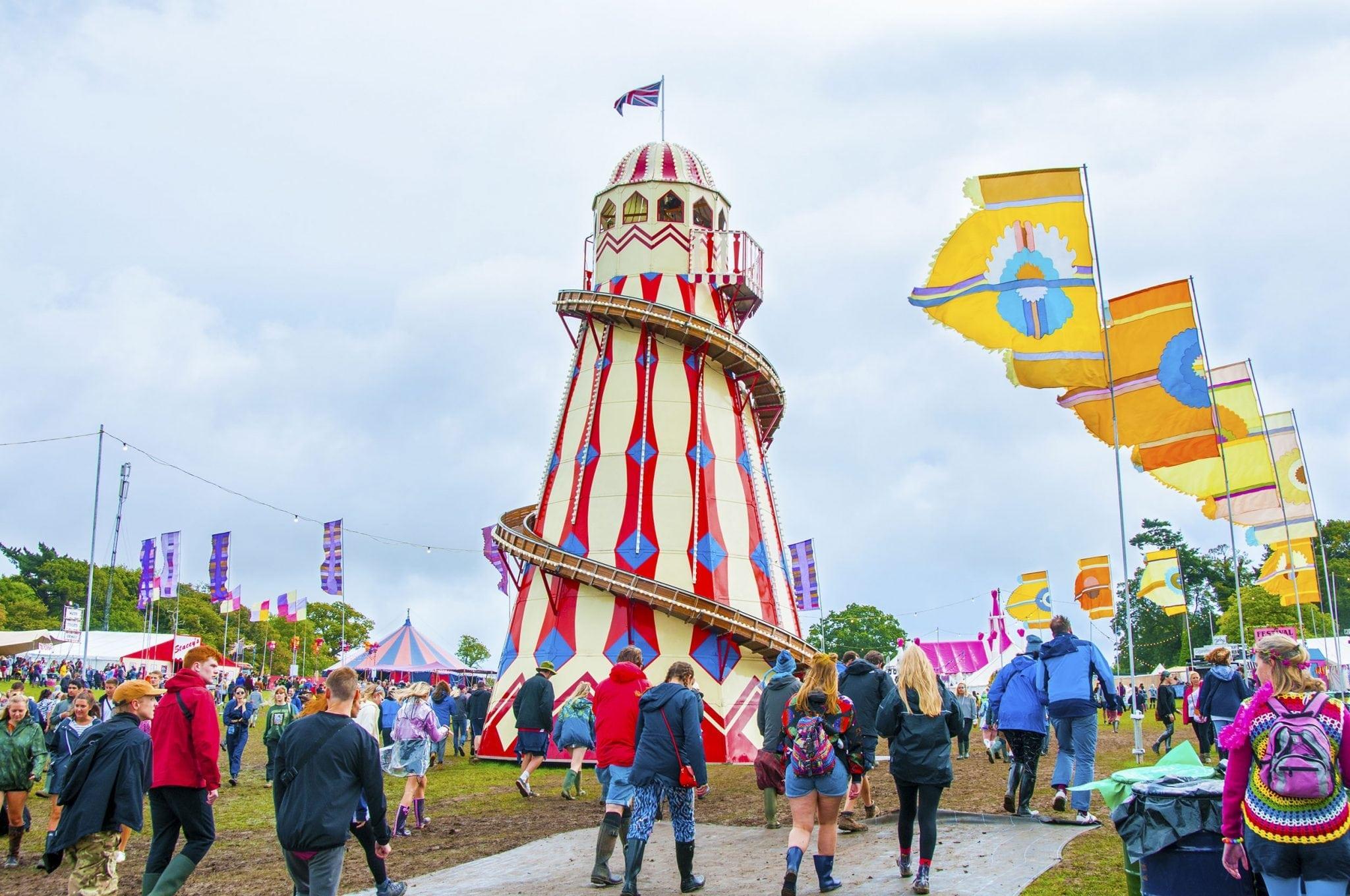 Several people walking towards a Helter Skelter ride at a festival in an open field