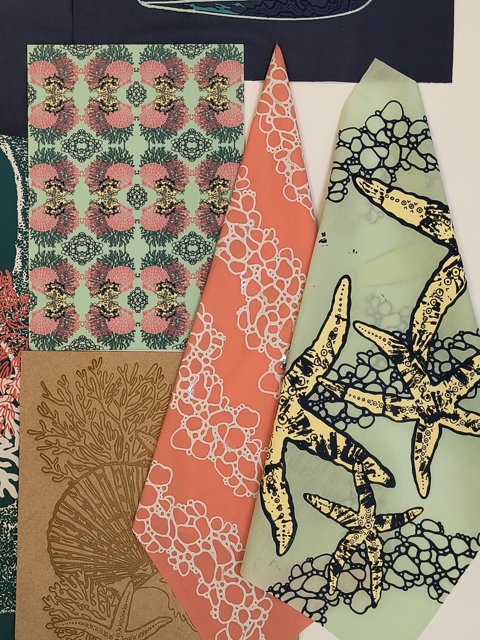 Mixed fabric or paper pieces with geometric patterns: coral with white circles, green with pink florals, brown tree motifs, pale green with yellow starfish and black coral designs.
