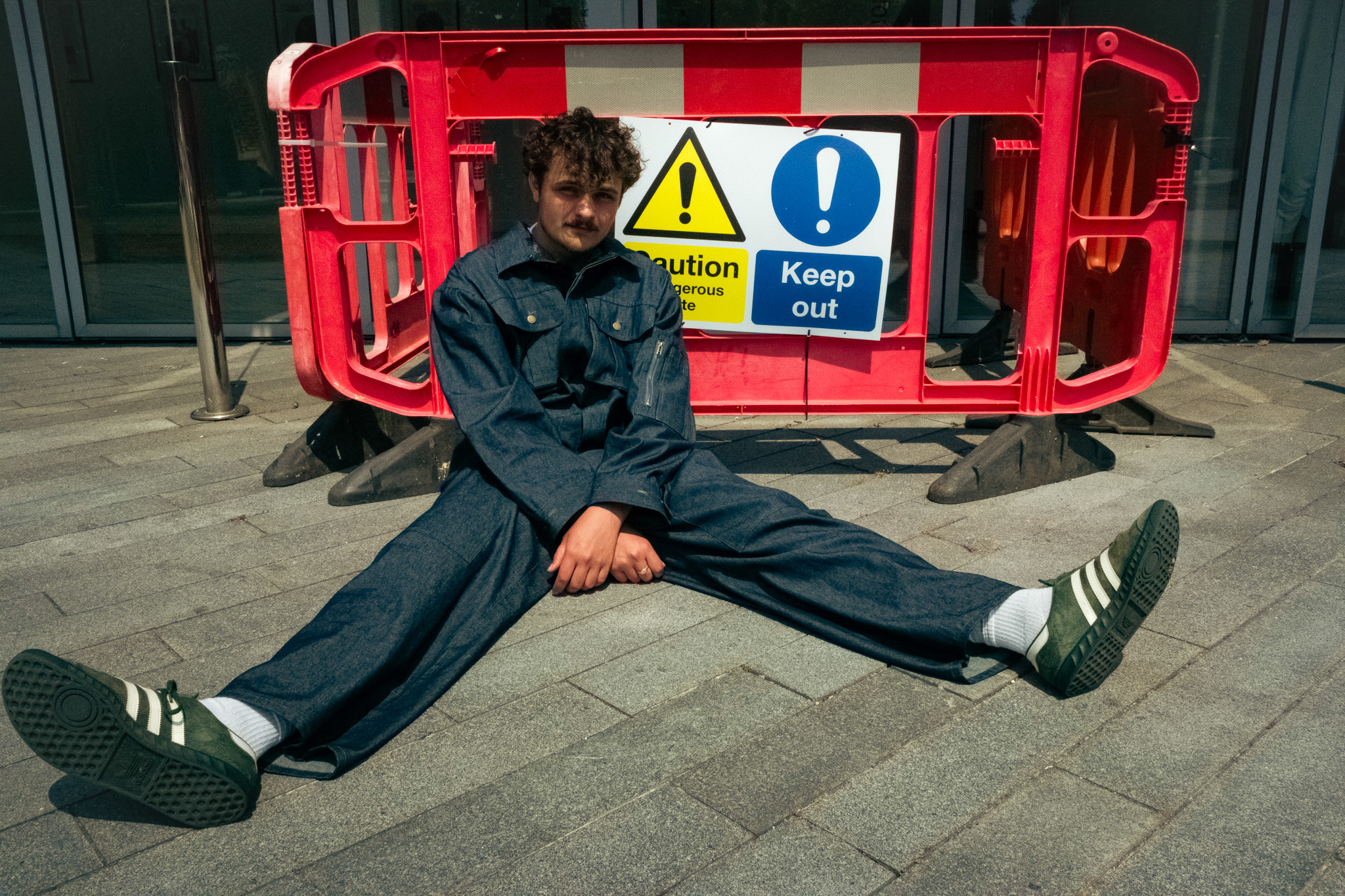 A man sat on the ground in a work-suit in front of a warning barricade