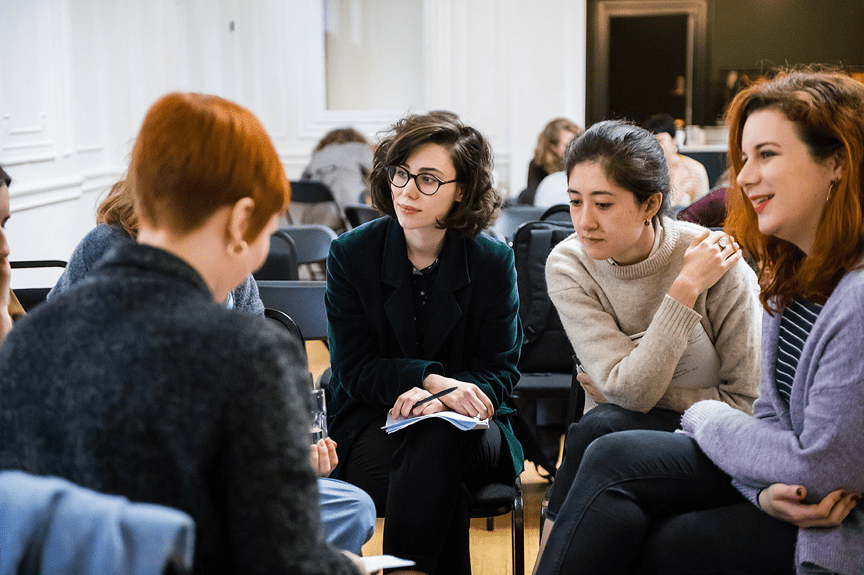 A small circle of people sit and discuss in a gallery space