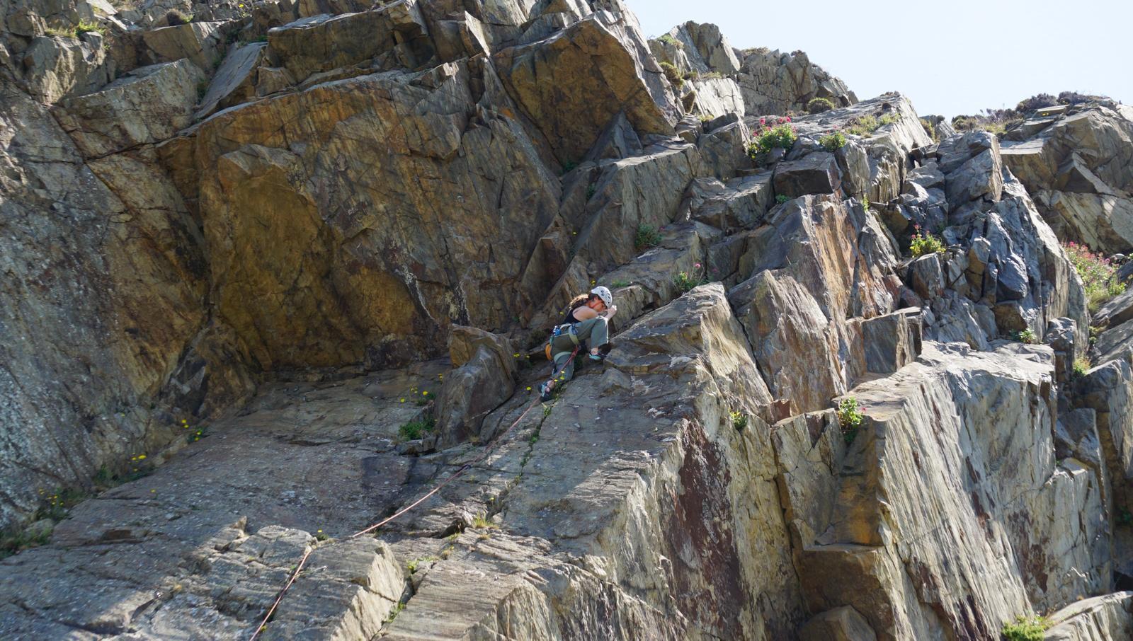 Jagged rock formations with layered grey and brown stone, patches of green moss, under pale blue sky.