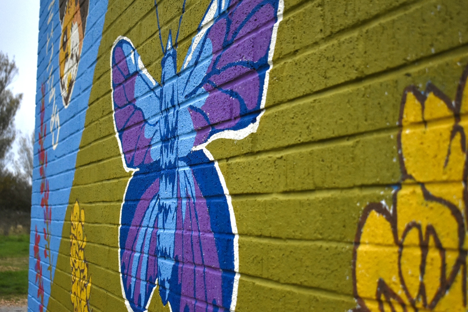 Colourful mural on wooden wall featuring large purple and blue butterfly with yellow flowers painted on horizontal planks.