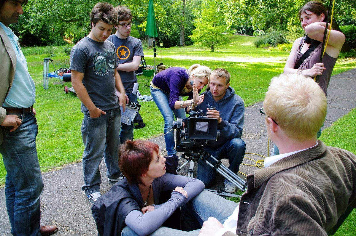 Group of people in a park. One of them is crouched down by a film camera.