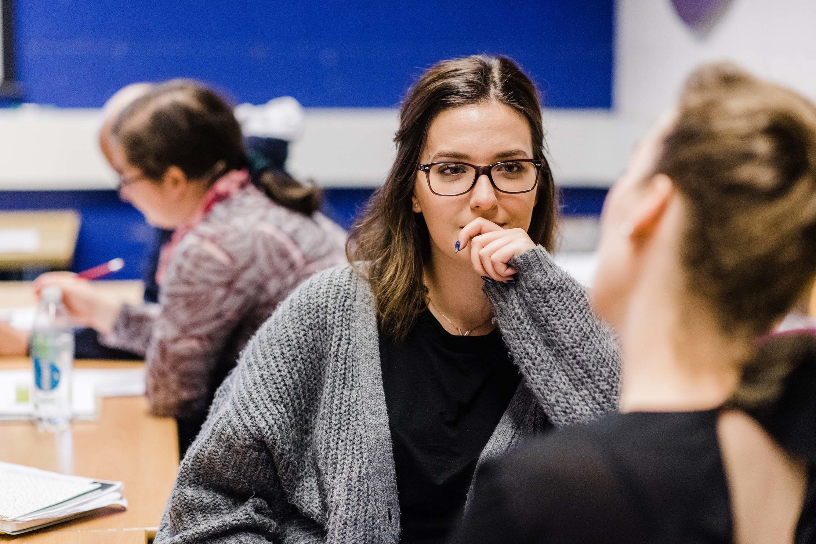 Close-up of a student in conversation with another student while sitting in a classroom.