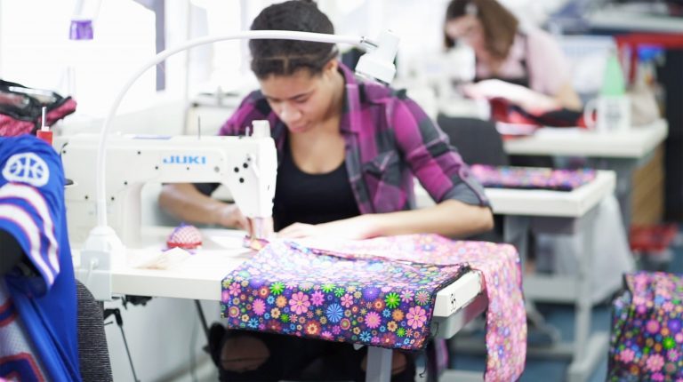 A person sits at a sewing machine and works on a colourful piece of fabric