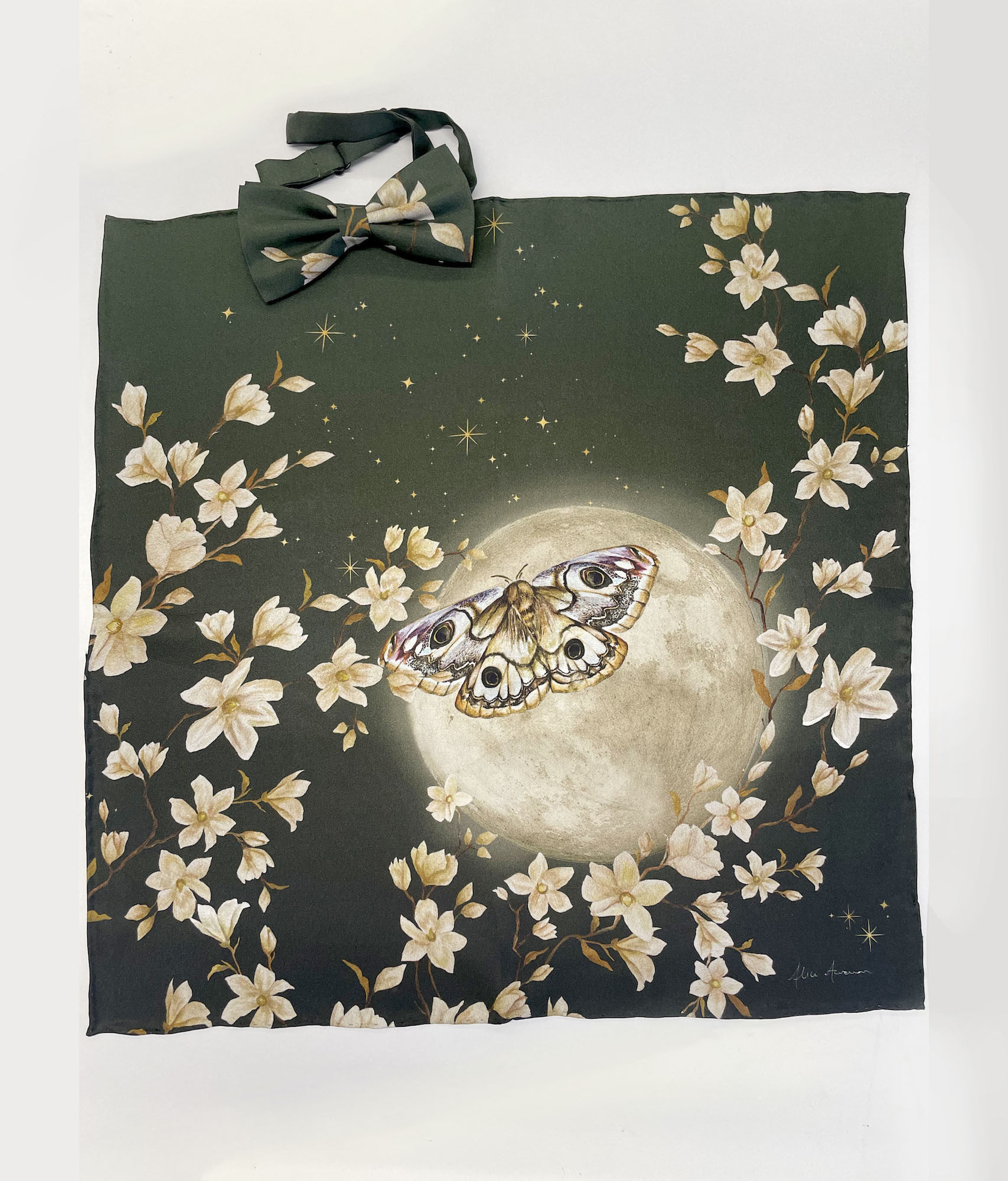 A green pocket square with a white floral, moon and butterfly pattern on a plain background. A matching bow tie lies just above the pocket square.