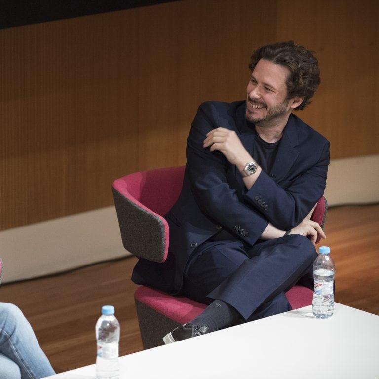 Edgar Wright seated in front of a desk smiling during an interview.
