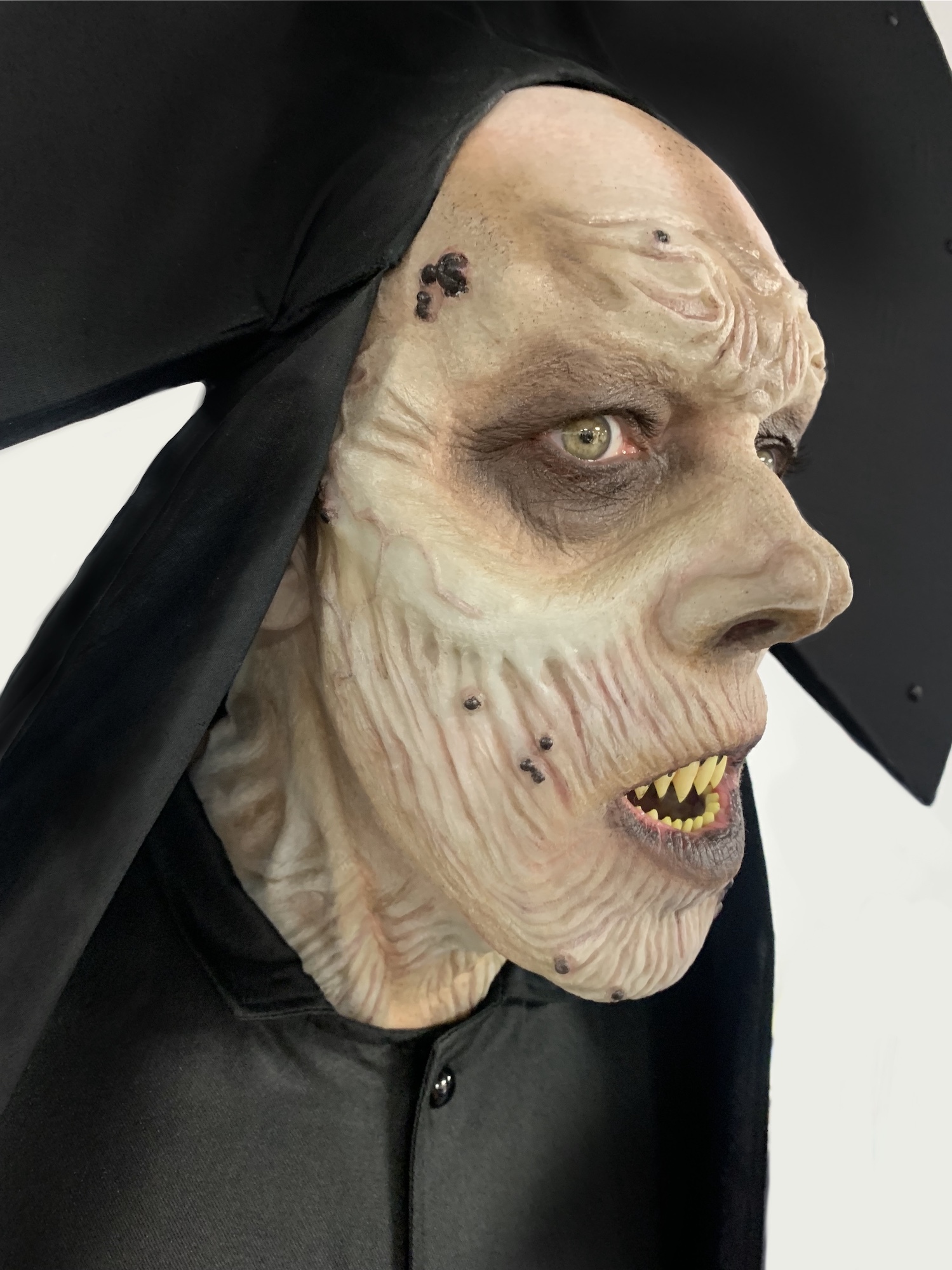 Close-up of a man's face with heavy horror-themed prosthetics, wearing a black headdress and robes.