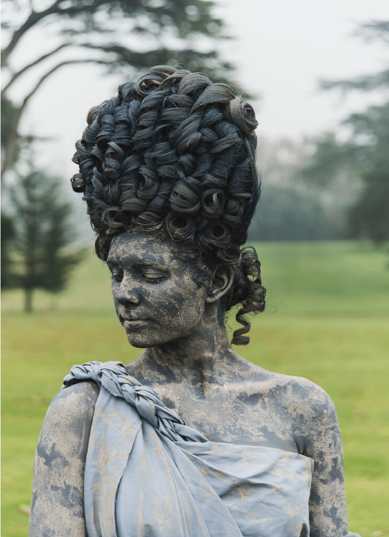 A person made up and dressed to look like a stone statue with a toga and high wig.