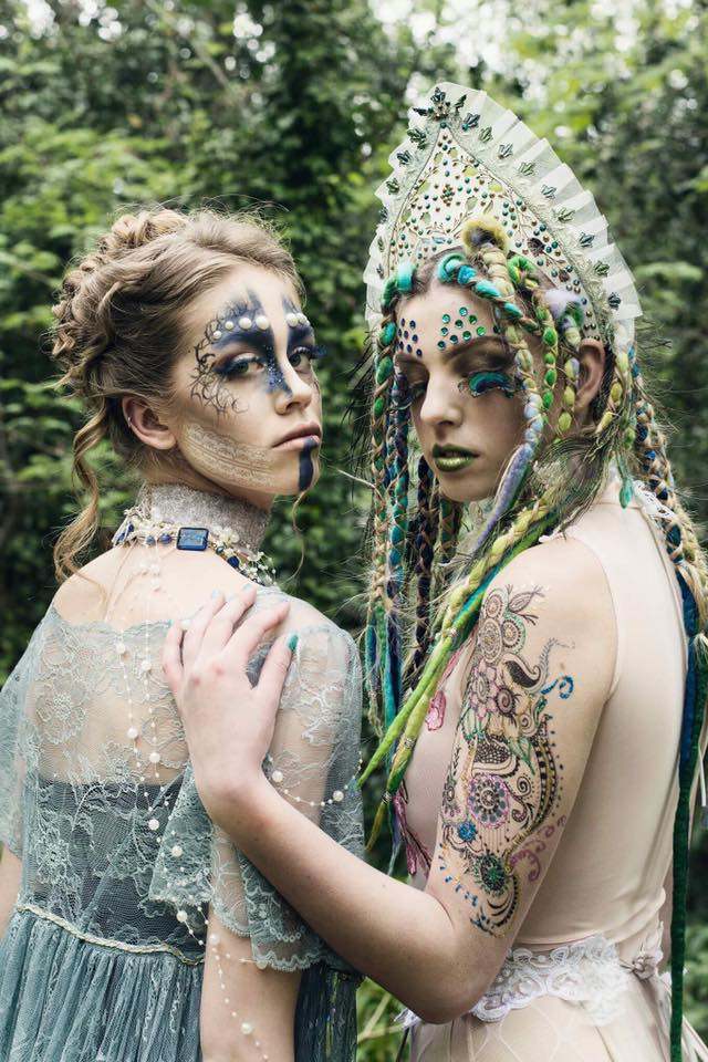 Two people in elaborate facial make-up, tattoos and headdress look over their shoulders towards the camera.