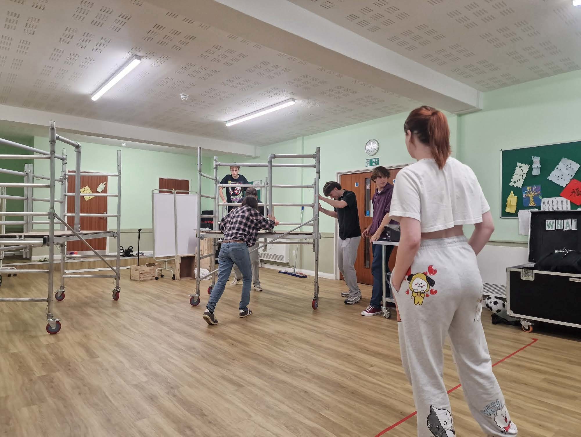 Rebecca McKinnon working with actors as fighting captain, back turned away from the camera, actors working around construction-like set design.