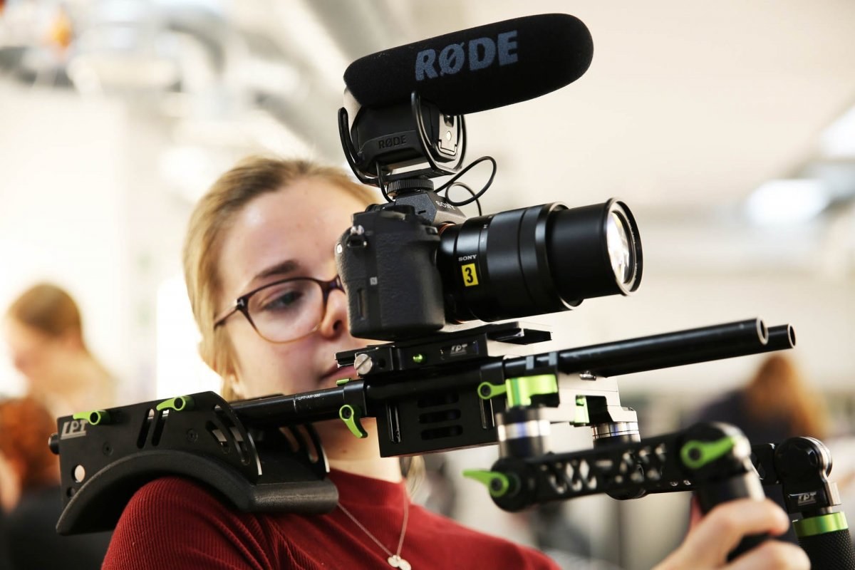Close-up of a person operating a camera attached to a rig on their shoulder.