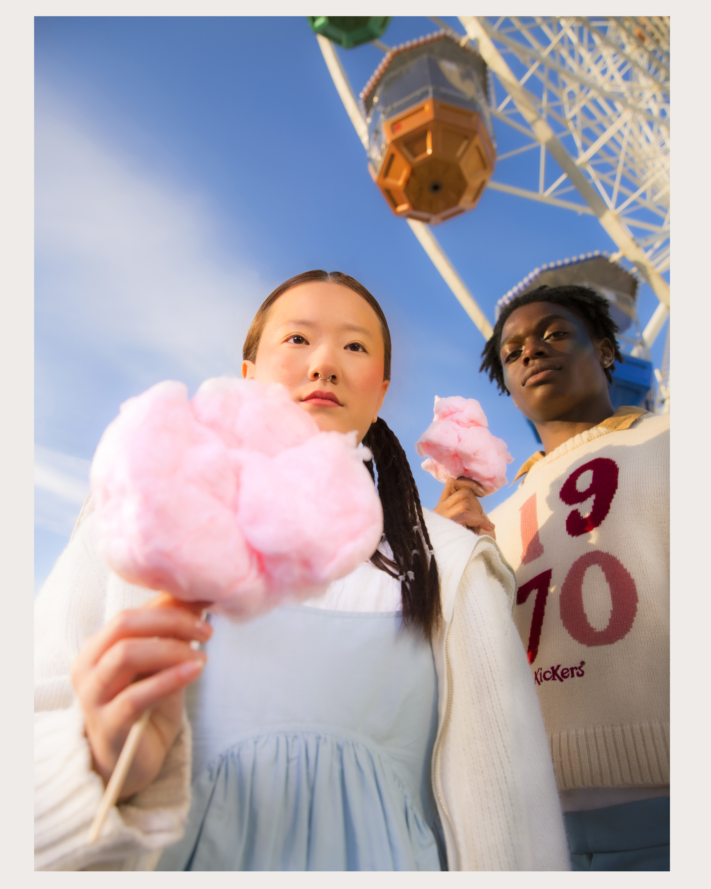 A dreamy scene of two models holding candy floss in front of a ferris wheel from below.