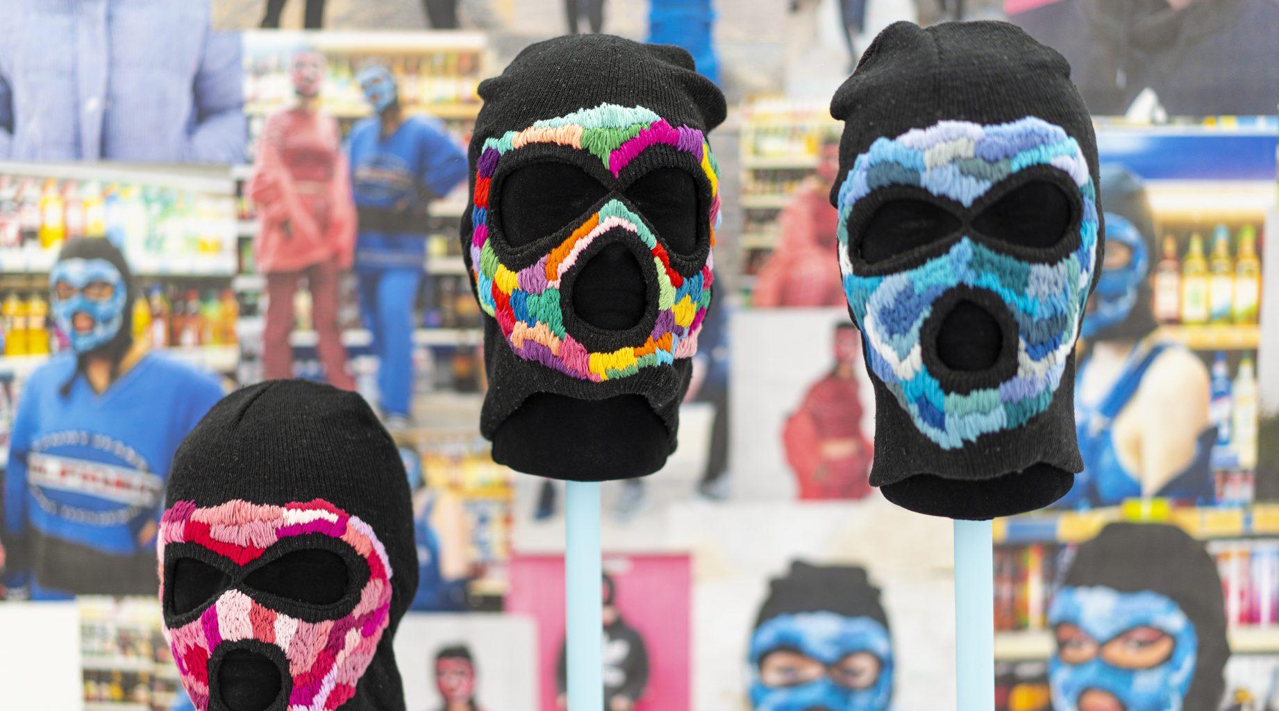 Three brightly coloured balaclava masks on stands.